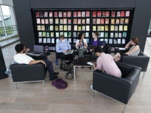 Six personnes assises en cercle discutent entre elles devant un mur de livres colorés.